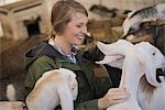 A woman in a stable on an organic farm.  White and black goats.