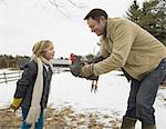 A man holding a chicken in his hands. A girl leaning forwards. Farm in the snow.