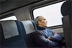 A mature man sitting in a window seat on a train journey, looking out into the distance.