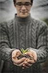 A person in a commercial glasshouse, holding a small plant seedling in his cupped hands.