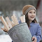 An organic farm in winter in New York State, USA. A girl carrying a bucket full of kindling and firewood.