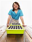 A young girl leaning on a table with two tray of freshly planted seeds resting on dark organic soil.