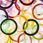 A large group of multi-colored condoms displayed on a white background. Heaped up.