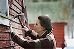 An organic farm in upstate New York, in winter. A woman with a hammer repairing the shingles on a barn.