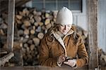 An organic farm in upstate New York, in winter. A woman in sheepskin coat and woollen hat using a cell phone.