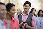 People outdoors in the city in spring time. New York City park. A group of men and women, and one young man holding a mobile phone.