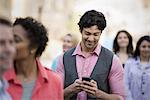 People outdoors in the city in spring time. A group of men and women. A man looking at his cell phone.