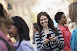 People outdoors in the city in spring time. New York City park. A young woman holding a mobile phone, and looking up at the camera.
