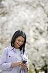 Outdoors in the city in spring time. New York City park. White blossom on the trees. A young woman checking her mobile phone and smiling.