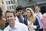 People outdoors in the city in spring time. New York City. A group of men and women, a couple at the centre looking at a cell phone.