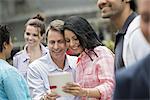 People outdoors in the city in spring time. New York City. A group of men and women, a couple in the centre looking at a digital tablet screen.