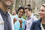 People outdoors in the city in spring time. New York City park. Two women in a group of friends, looking at a cell phone and smiling.