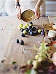 A woman at a domestic kitchen table. Arranging fresh fruit, black and green figs on a cheese board. Organic food. From farm to plate.