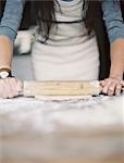 A domestic kitchen. A woman preparing a meal. Rolling out pastry on a table top.