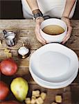 A domestic kitchen tabletop. A stack of white plates and fresh pears and a stack of sugar cubes. A bowl of  fudge sauce.