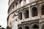 A woman outside the Colosseum amphitheatre in Rome, taking photographs.