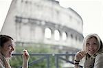 Two women seated on a terrace overlooking the huge Roman amphitheatre building, the Colosseum in Rome.