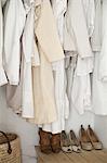 A closet with cream and white clothes, jackets, shirts and tunics hanging up. A row of women's shoes arranged neatly on the floor.