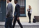 Young people outdoors on the city streets in springtime. A woman on her own, and two men walking past on the cobbled street.