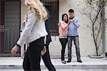 Young people outdoors on the city streets in springtime. A couple taking images of themslves using a smart phone.  Two people walking by.