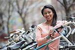 City life in spring. Young people outdoors in a city park. A young woman with black hair, wearing a peach coloured shirt, standing beside a rack of parked locked bicycles.