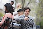 City life in spring. Young people outdoors in a city park. Sitting on a park bench. Five people, men and women, checking their phones.