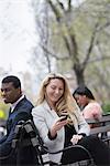 City life in spring. Young people outdoors in a city park. Three people sitting on a bench. Two checking their phones.