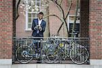 City life in spring. Young people outdoors in a city park. A man in a suit, beside a bicycle park on a sidewalk. Using his smart phone.