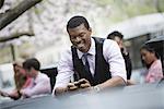 City life in spring. Young people outdoors in a city park. A man sitting down checking his smart phone, with four people in the group behind him.