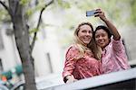 City life in spring. Young people outdoors in a city park. Two women taking a self portrait or selfy with a smart phone.