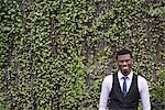 City life in spring. City park with a wall covered in climbing plants and ivy.  A young man in a waistcoat, shirt and tie. Looking at the camera.