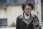 A woman wearing glasses, looking at her smart phone, keeping in touch while on the go.