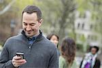 A group of people in a city park. A man in a grey sweater, checking his phone.