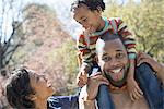 A New York city park in the spring. Sunshine and cherry blossom. A father carrying his son on his shoulders.