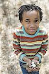 A New York city park in the spring. A small boy in a striped shirt, holding a nest with three birds eggs.