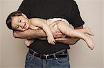 A young boy wearing cloth diapers being held by his father in his arms.