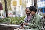 Outdoors in the city in spring. An urban lifestyle. A couple sitting side by side and looking at a phone screen.