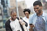 Outdoors in the city in spring. An urban lifestyle. A young man checking his phone and texting. A couple behind him.