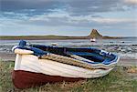 Fishing boat pulled onto the shore at Holy Island, looking towards the castle, Lindisfarne, Northumberland, England, United Kingdom, Europe