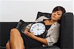 Portrait of Mid-Adult Woman Sleeping on Sofa and holding Alarm Clock