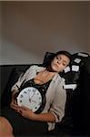 Portrait of Mid-Adult Woman Sleeping on Sofa and holding Alarm Clock surrounded by Speech Bubble Adhesive Notes