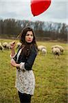Young Woman with Heart-shaped Balloon by Sheep in Field, Mannheim, Baden-Wurttemberg, Germany