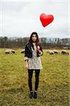 Young Woman with Heart-shaped Balloon by Sheep in Field, Mannheim, Baden-Wurttemberg, Germany