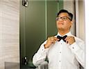 Portrait of Groom tying Bowtie before Wedding