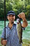 mid adult fisherman on holidays on river, relaxing and fishing trout. Focus on background