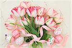 Tulip flower arrangement with easter eggs and ribbon curl over handmade paper background.