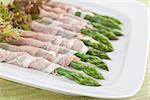 Prosciutto wrapped green asparagus with lollo rosso lettuce on a plate