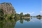 The rock, blue sky and green trees glassed in the water of Dalyan river (Turkey). Several boats are in the background.