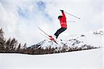 Male kid performs a high jump with the ski. Winter season, red jacket. Valle d'Aosta, Italy, Europe.