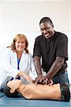 Adult first aid or EMT student practicing CPR on a dummy, with the help of a doctor or nurse.  Vertical with room for text.